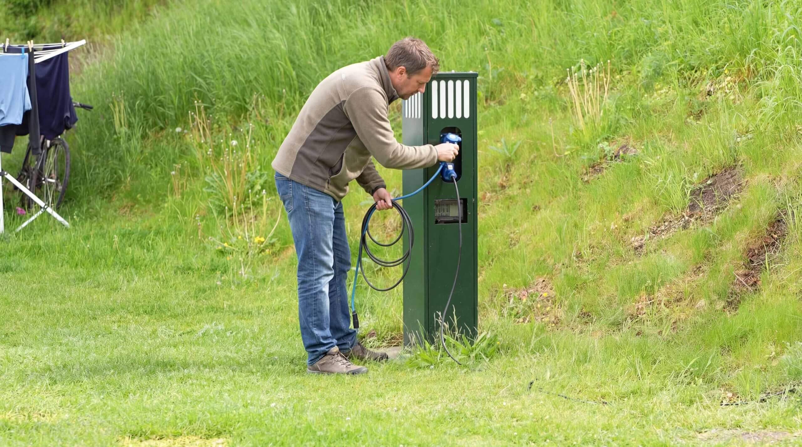Campist tilslutter strømkabel til en af GoCampings strømstandere på en campingplads i Danmark