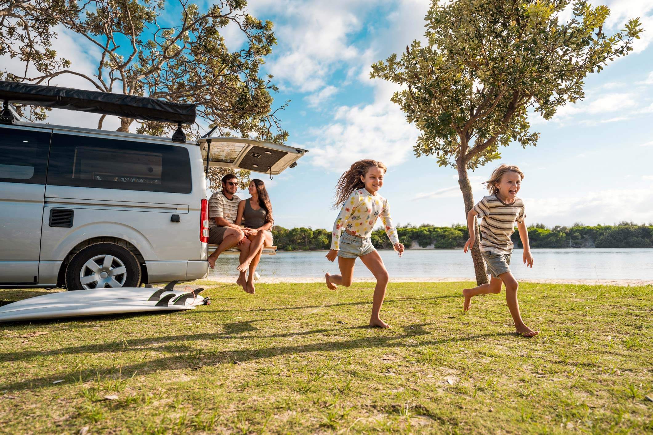 Glad familie i autocamper nyder sol og græs ved sø